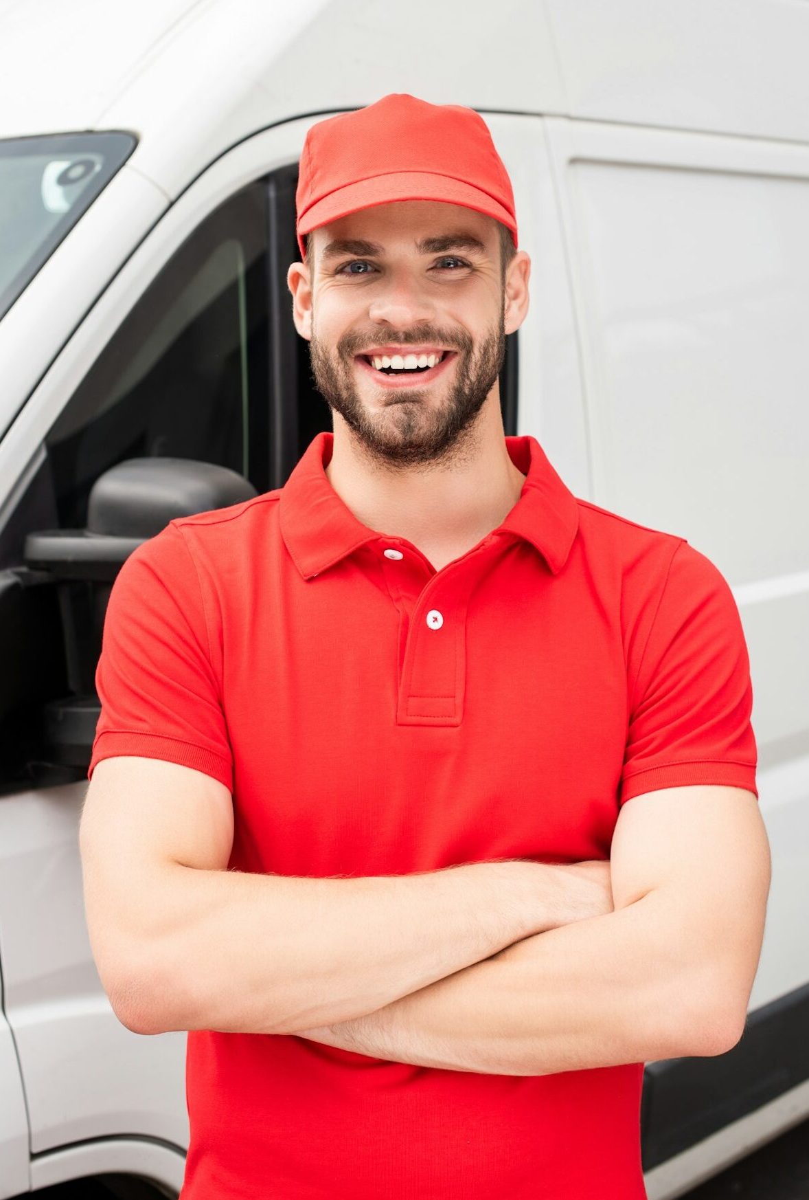 smiling caucasian delivery man standing with crossed arms and looking at camera near van